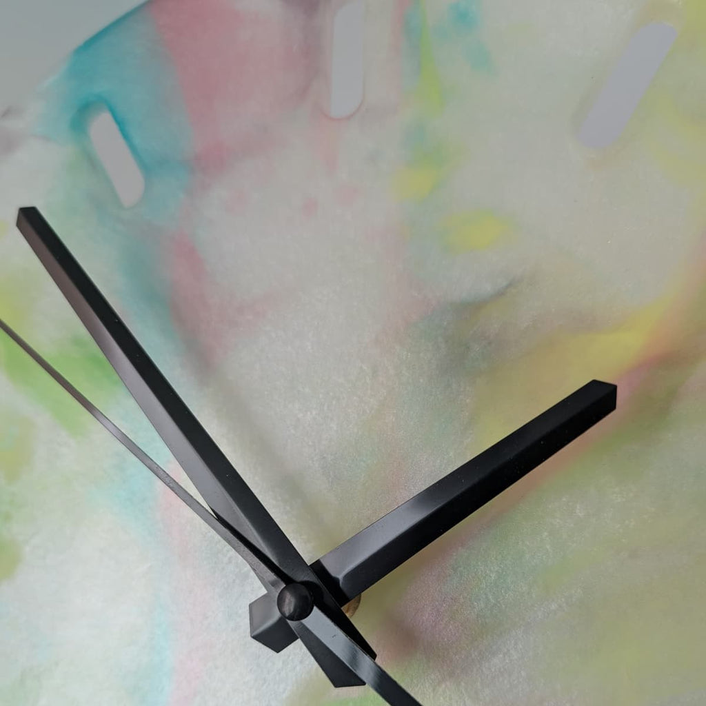 Reloj de resina hecho a mano por Siete Maderas. Fondo blanco nácar y multicolor. Diseño único. Agujas negras.