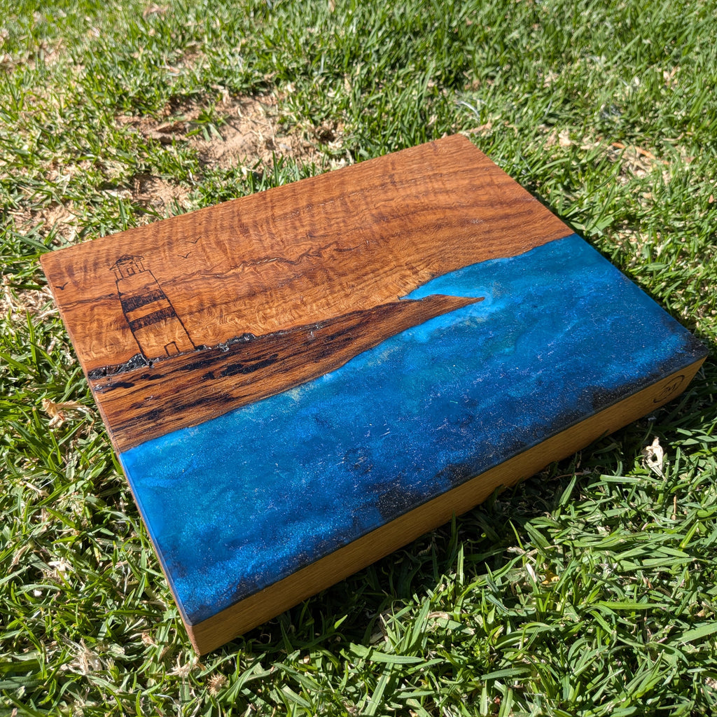 Tabla de servir El faro, hecha a mano por Siete Maderas en madera de roble, usando el nudo como parte del diseño y con detalles en resina simulando el mar y pirograbado dibujando un faro y unas gaviotas.