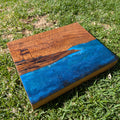 Tabla de servir El faro, hecha a mano por Siete Maderas en madera de roble, usando el nudo como parte del diseño y con detalles en resina simulando el mar y pirograbado dibujando un faro y unas gaviotas.