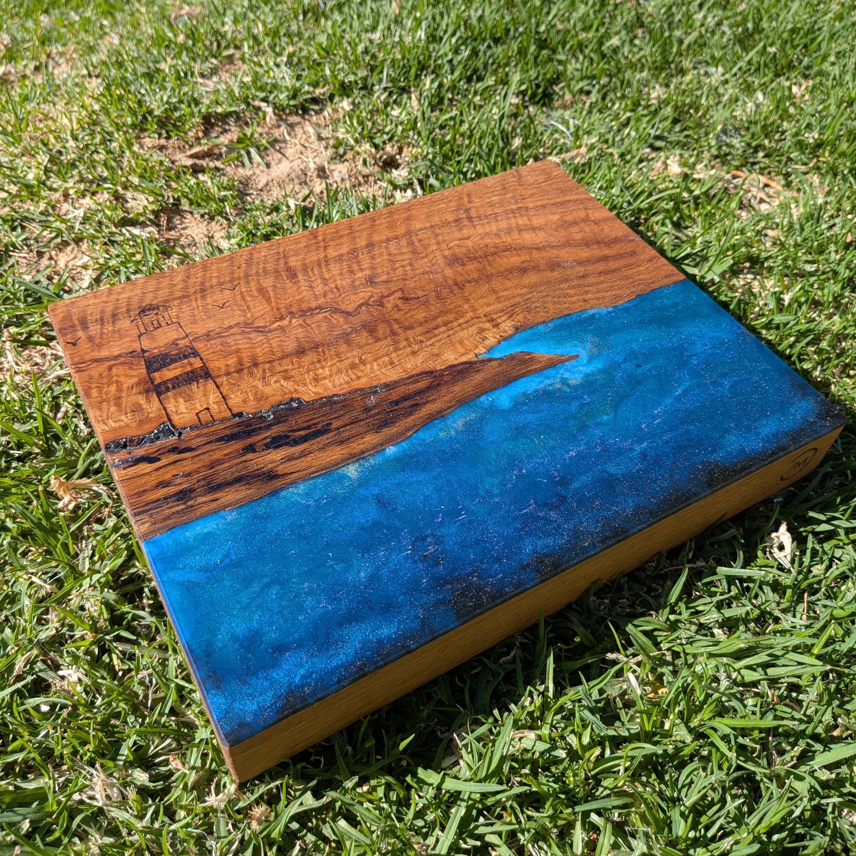 Tabla de servir El faro, hecha a mano por Siete Maderas en madera de roble, usando el nudo como parte del diseño y con detalles en resina simulando el mar y pirograbado dibujando un faro y unas gaviotas.
