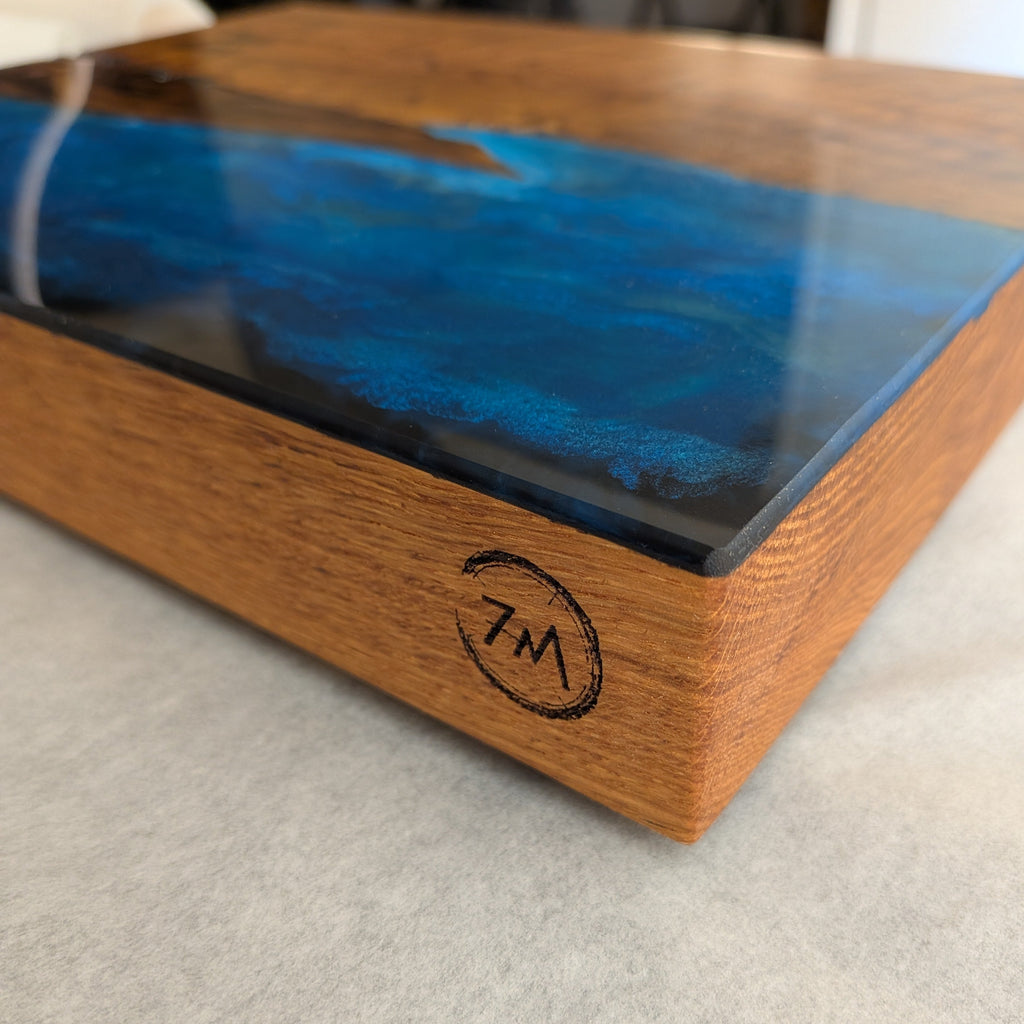 Tabla de servir El faro, hecha a mano por Siete Maderas en madera de roble, usando el nudo como parte del diseño y con detalles en resina simulando el mar y pirograbado dibujando un faro y unas gaviotas. Detalle logo.