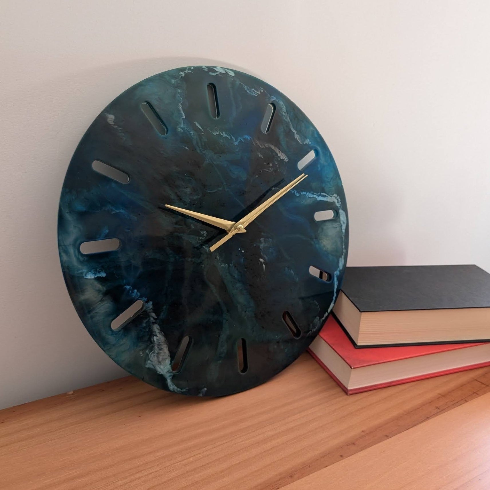 Decoración versátil con el reloj Skuld de resina azul con vetas blancas que evocan el mar. Agujas doradas. Es perfecto para una cómoda o estantería.