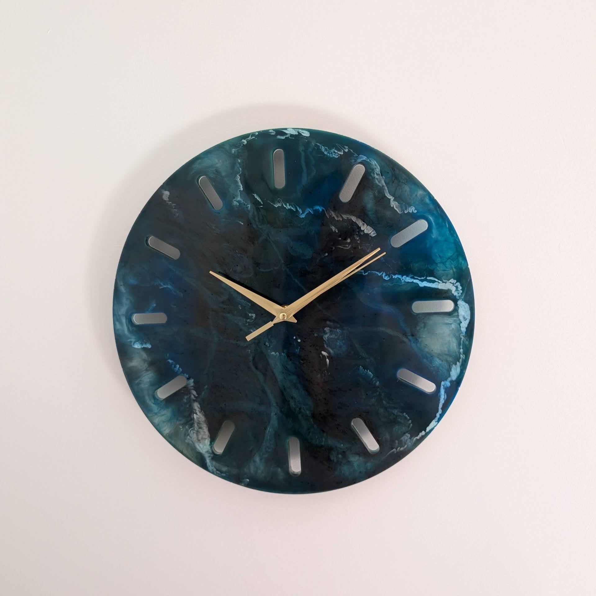 Reloj de pared redondo de resina Skuld, azul oscuro con vetas blancas que evocan el mar profundo. Agujas doradas, diseño abstracto. Una decoración única para cualquier espacio.